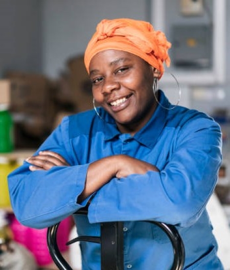 Mid adult african woman with hand pallet standing in a distribution warehouse. Portrait of a happy afro woman with headscarf, wearing uniform, working in a factory warehouse.
